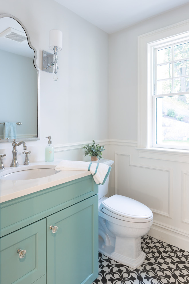 Inredning av ett klassiskt mellanstort vit vitt toalett, med luckor med infälld panel, turkosa skåp, en toalettstol med separat cisternkåpa, vita väggar, cementgolv, ett undermonterad handfat, bänkskiva i kvarts och flerfärgat golv