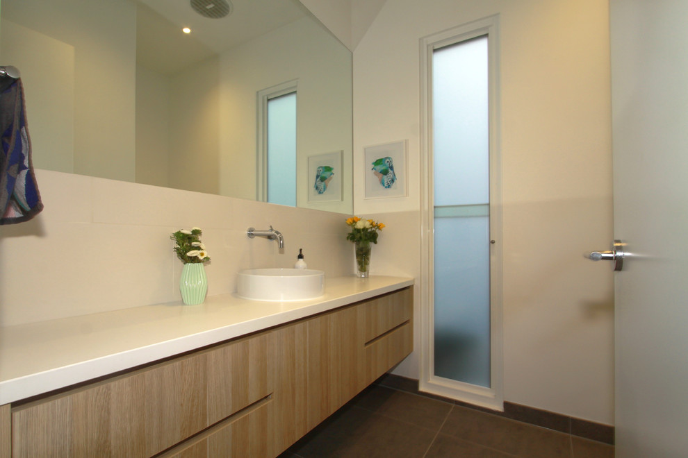 Idee per un bagno di servizio minimalista con ante lisce, ante in legno chiaro, piastrelle bianche, piastrelle in gres porcellanato, pareti bianche, lavabo a bacinella, top in superficie solida e pavimento marrone