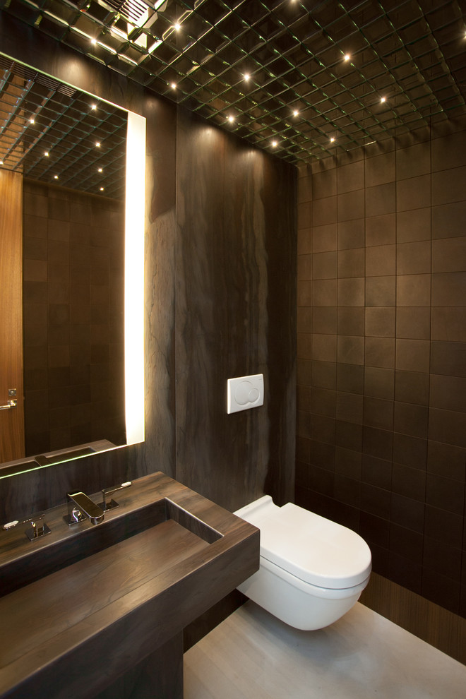Modern inredning av ett litet toalett, med marmorbänkskiva, en vägghängd toalettstol, brun kakel, bruna väggar, kalkstensgolv, ett integrerad handfat och kakelplattor