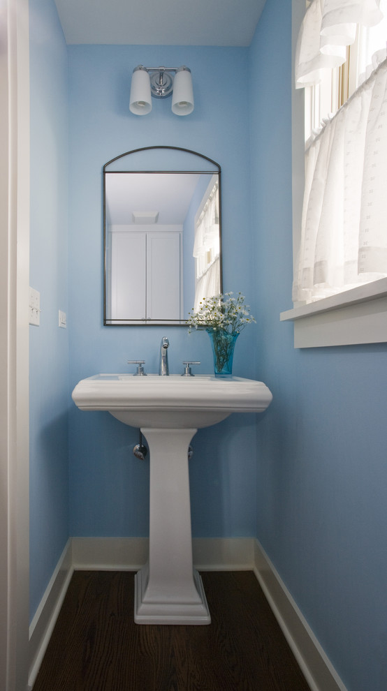Imagen de aseo tradicional pequeño con sanitario de dos piezas, paredes azules, suelo de madera en tonos medios, lavabo con pedestal y suelo marrón