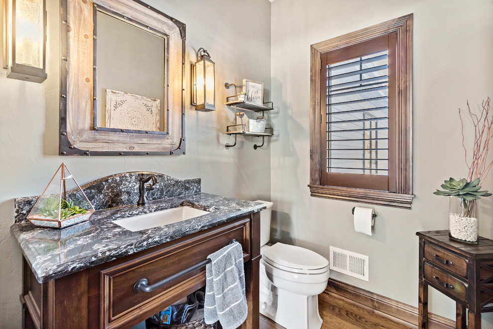 This is an example of a medium sized rustic cloakroom in Charleston with freestanding cabinets, dark wood cabinets, a two-piece toilet, beige walls, medium hardwood flooring, a submerged sink and brown floors.
