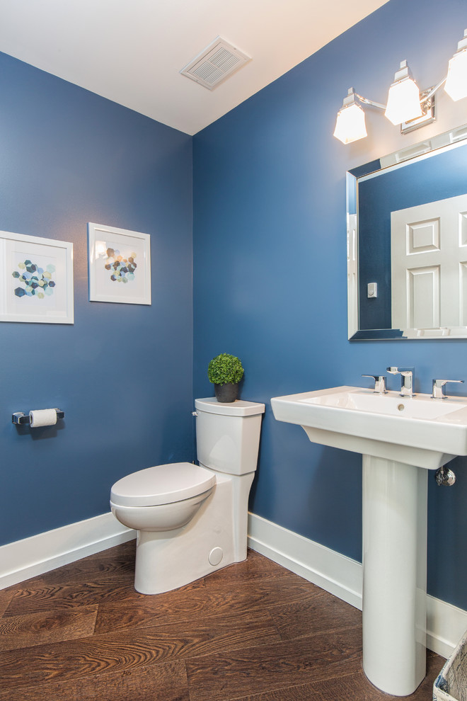 Inredning av ett modernt toalett, med en toalettstol med separat cisternkåpa, blå väggar, mörkt trägolv och ett piedestal handfat