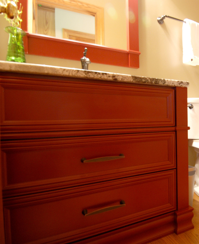 Diseño de aseo pequeño con puertas de armario rojas, sanitario de dos piezas, paredes beige, suelo de madera en tonos medios, lavabo bajoencimera, encimera de granito y armarios con paneles empotrados