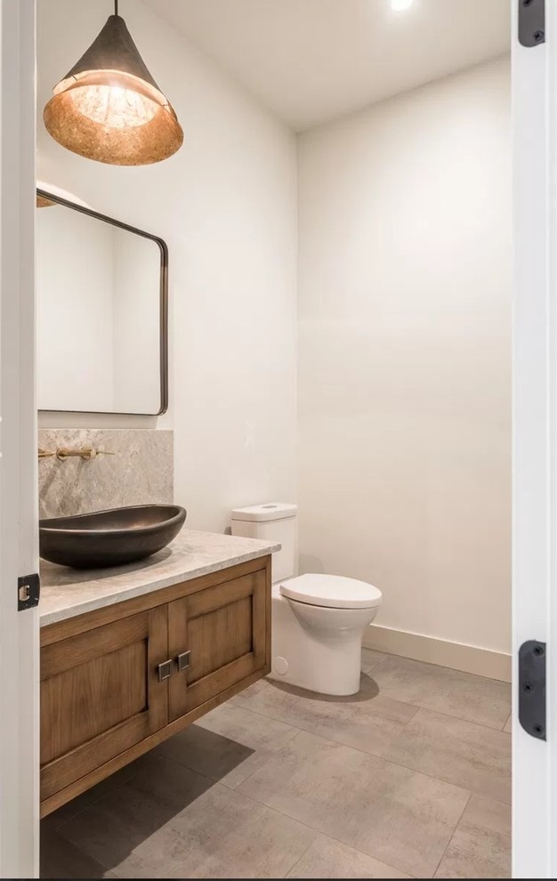 This is an example of a medium sized cloakroom in Sacramento with shaker cabinets, distressed cabinets, a one-piece toilet, white walls, porcelain flooring, a vessel sink, granite worktops, grey floors and beige worktops.