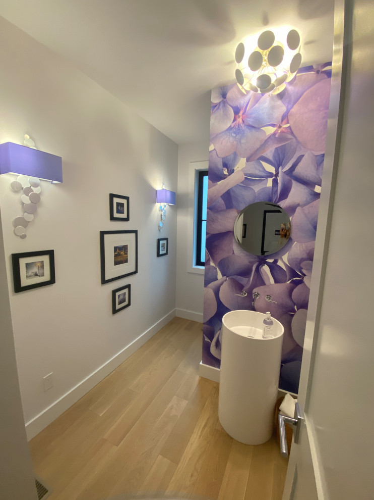 Mid-sized transitional light wood floor, white floor and wallpaper powder room photo with white cabinets, a one-piece toilet, a freestanding vanity, purple walls and a pedestal sink