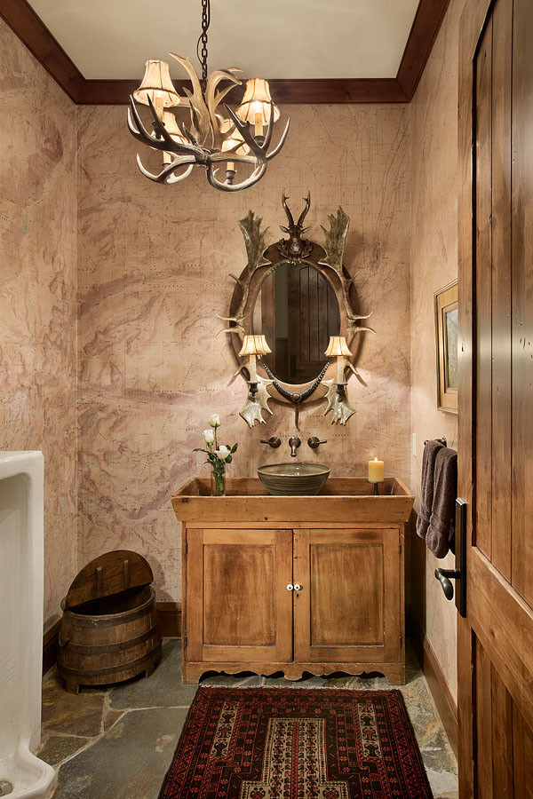 Foto på ett stort rustikt toalett, med möbel-liknande, skåp i ljust trä, ett urinoar, ett fristående handfat, träbänkskiva, flerfärgade väggar, skiffergolv och flerfärgat golv