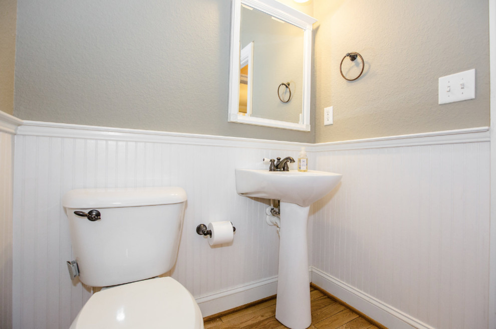 Idéer för att renovera ett maritimt vit vitt toalett, med en toalettstol med separat cisternkåpa, beige väggar, ljust trägolv, ett piedestal handfat och brunt golv
