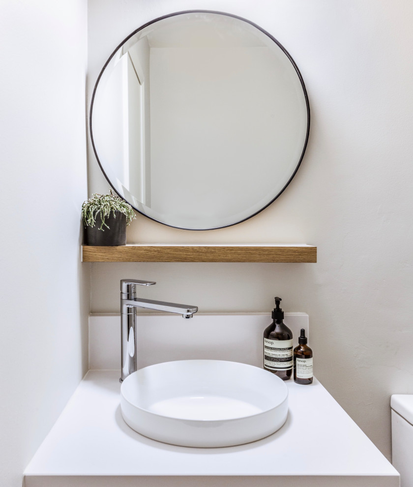 Kleine Moderne Gästetoilette mit weißen Fliesen, weißer Wandfarbe, braunem Holzboden, Aufsatzwaschbecken, Quarzwerkstein-Waschtisch und weißer Waschtischplatte