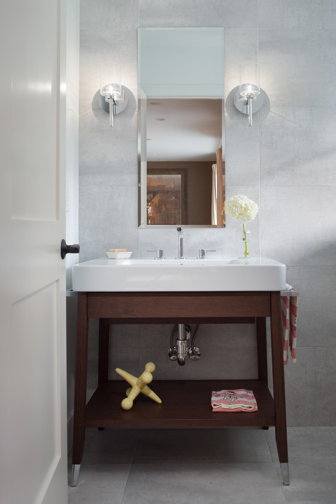 Inredning av ett modernt litet toalett, med ett fristående handfat, öppna hyllor, skåp i mörkt trä, en toalettstol med hel cisternkåpa, grå kakel, keramikplattor, grå väggar, klinkergolv i keramik och grått golv