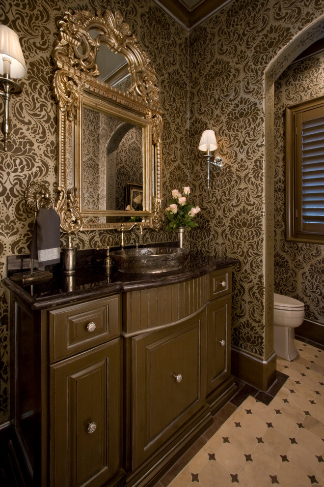 На фото: большой туалет в классическом стиле с настольной раковиной, фасадами с выступающей филенкой, коричневыми фасадами, столешницей из гранита, унитазом-моноблоком, бежевой плиткой и полом из травертина