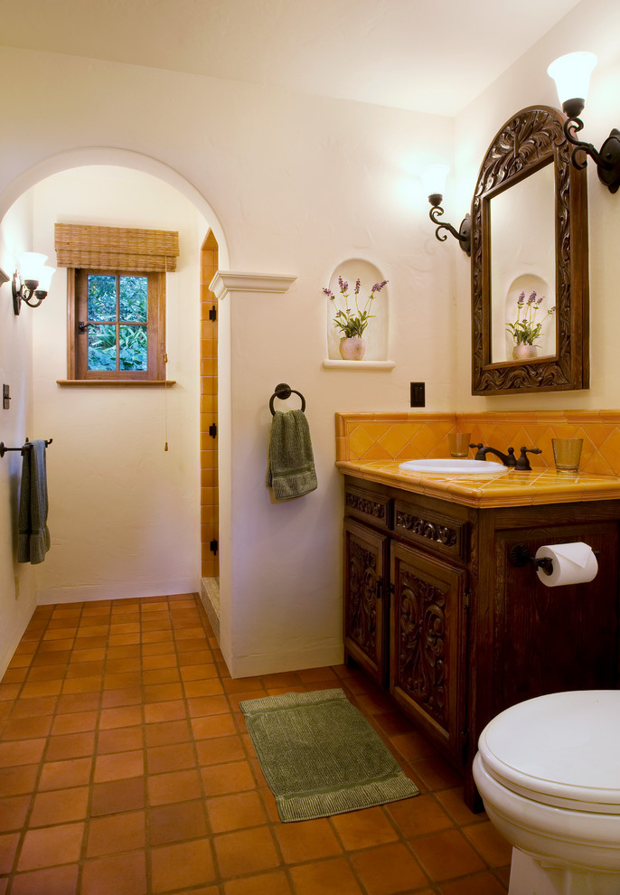 Inredning av ett medelhavsstil toalett, med ett nedsänkt handfat, möbel-liknande, skåp i mörkt trä, kaklad bänkskiva, orange kakel, keramikplattor, vita väggar och klinkergolv i terrakotta