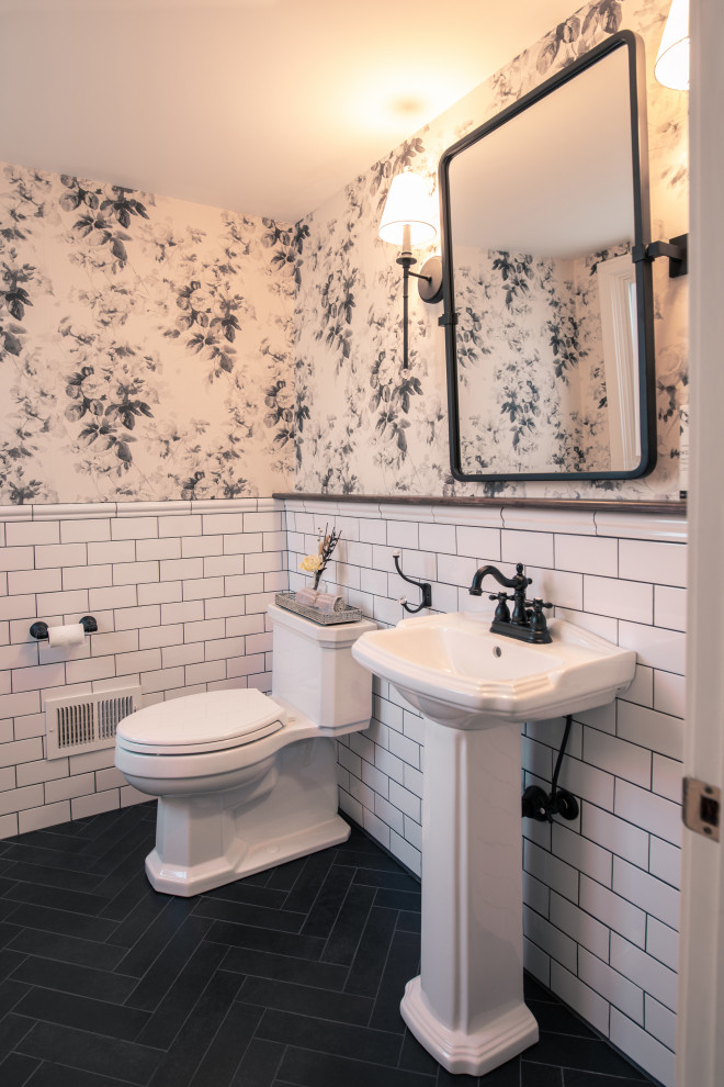 Lantlig inredning av ett mellanstort toalett, med vita skåp, en toalettstol med hel cisternkåpa, vit kakel, keramikplattor, klinkergolv i porslin, ett piedestal handfat och svart golv