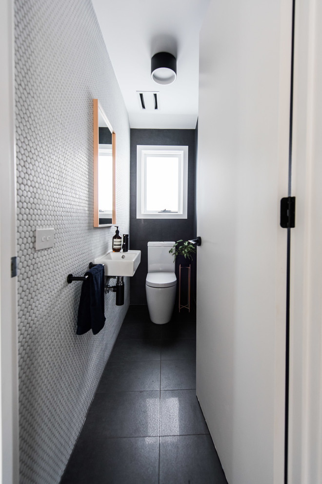 Immagine di un bagno di servizio contemporaneo con WC monopezzo, pistrelle in bianco e nero, piastrelle a mosaico, pavimento in gres porcellanato, lavabo sospeso e pavimento nero