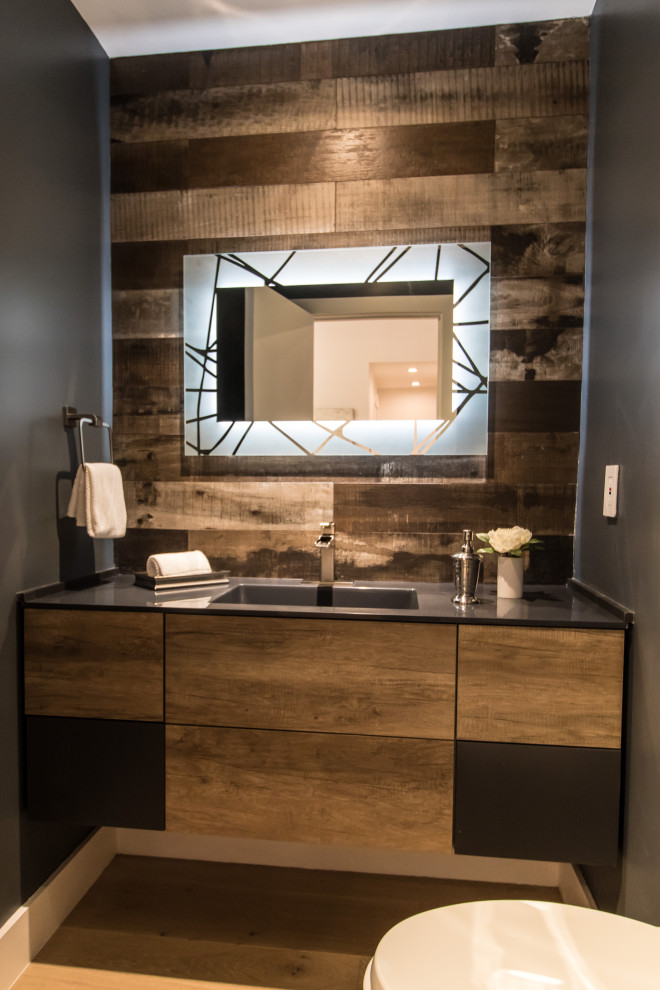 Medium sized contemporary cloakroom in Los Angeles with flat-panel cabinets, medium wood cabinets, a one-piece toilet, black walls, light hardwood flooring, an integrated sink, engineered stone worktops, beige floors, black worktops, a floating vanity unit and wood walls.