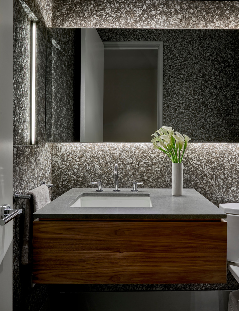 Cette image montre un WC et toilettes design en bois brun de taille moyenne avec un placard à porte plane, WC à poser, un mur gris, un lavabo encastré et un plan de toilette en quartz.