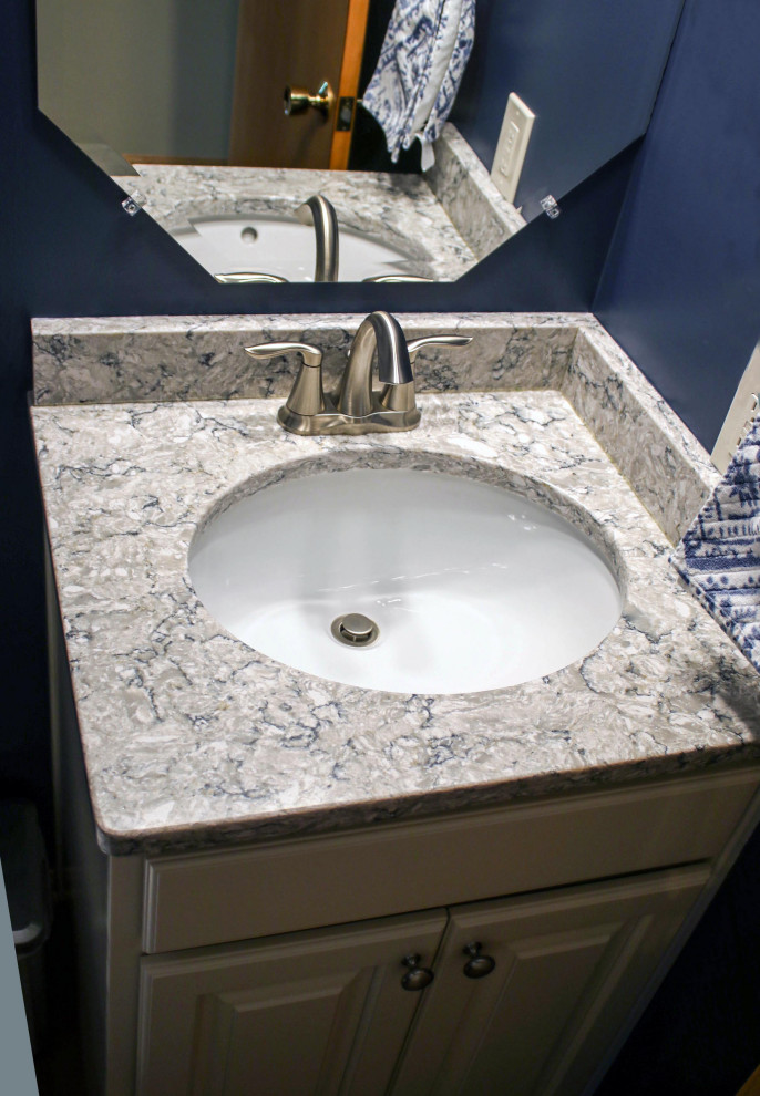 Small transitional vinyl floor powder room photo in Cleveland with raised-panel cabinets, a two-piece toilet, blue walls, an undermount sink, quartz countertops, beige countertops and a freestanding vanity