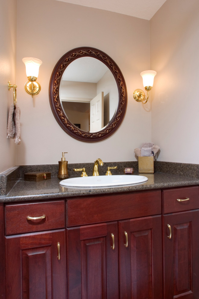 Cette image montre un petit WC et toilettes traditionnel en bois brun avec un lavabo posé, un placard avec porte à panneau surélevé, un plan de toilette en granite, WC séparés, un mur beige et un sol en bois brun.