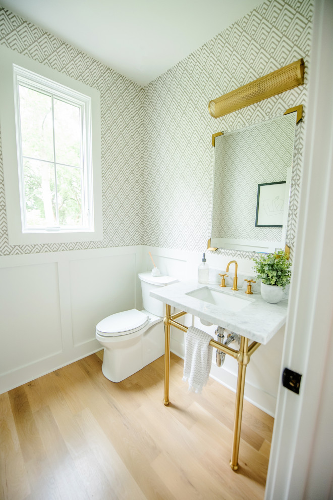 Contemporary cloakroom in Cincinnati with a two-piece toilet, white walls, light hardwood flooring, a wall-mounted sink, marble worktops, white worktops, a freestanding vanity unit and wallpapered walls.