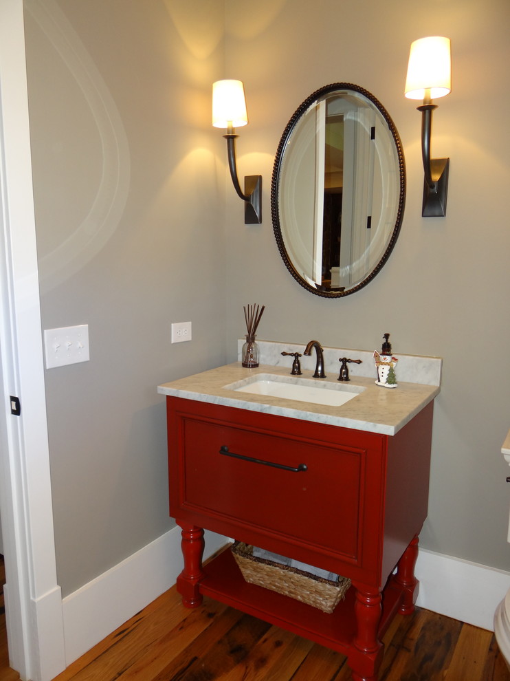Exemple d'un WC et toilettes nature de taille moyenne avec un lavabo encastré, un placard avec porte à panneau encastré, des portes de placard rouges, un plan de toilette en marbre, un mur gris et un sol en bois brun.