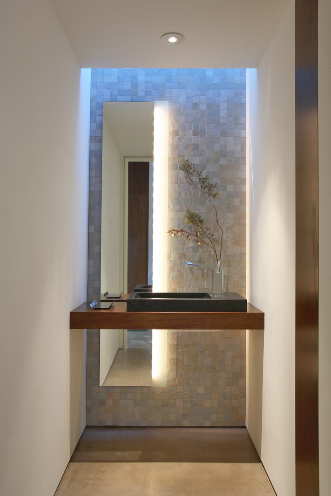 На фото: туалет в современном стиле с бежевой плиткой, каменной плиткой, белыми стенами, настольной раковиной, столешницей из дерева, бетонным полом и коричневой столешницей с