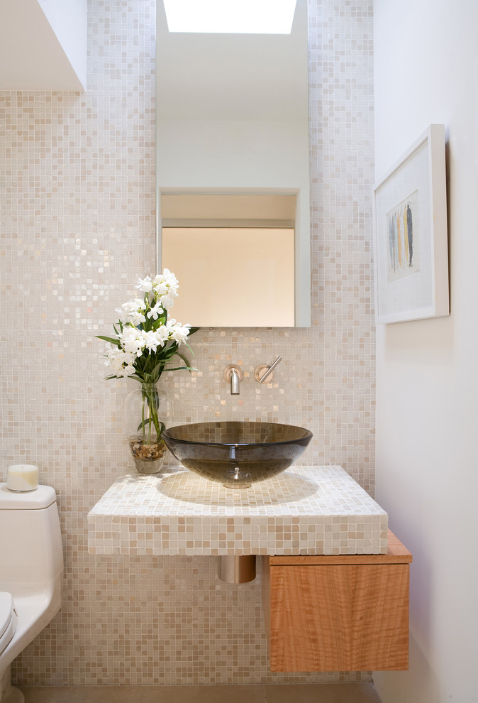Moderne Gästetoilette mit hellen Holzschränken, Toilette mit Aufsatzspülkasten, beigen Fliesen, Mosaikfliesen, weißer Wandfarbe, Aufsatzwaschbecken, gefliestem Waschtisch und flächenbündigen Schrankfronten in Los Angeles