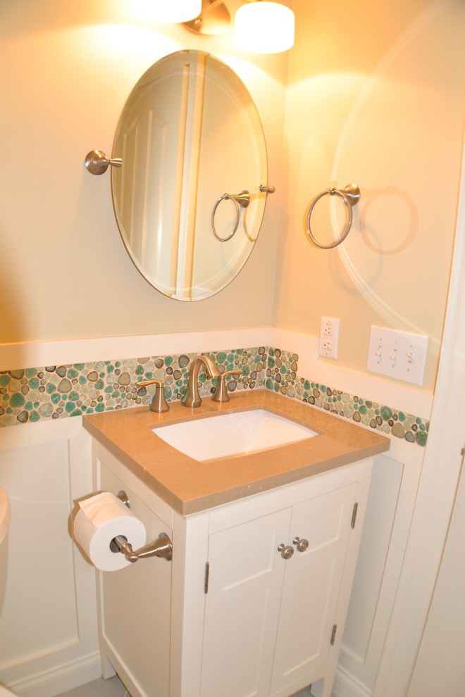 Amerikansk inredning av ett litet toalett, med ett undermonterad handfat, vita skåp, bänkskiva i akrylsten, en toalettstol med separat cisternkåpa, flerfärgad kakel, kakel i småsten, beige väggar, klinkergolv i porslin och luckor med infälld panel