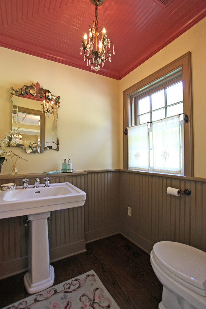 Immagine di un bagno di servizio country con WC monopezzo, lavabo a colonna, pareti gialle e parquet scuro