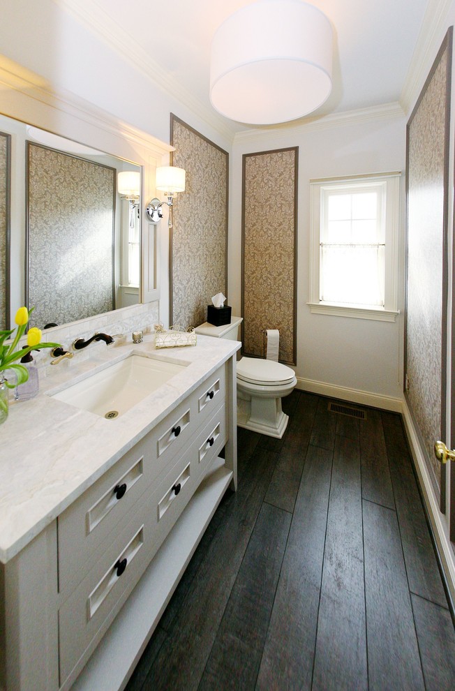 Inredning av ett klassiskt mellanstort vit vitt toalett, med möbel-liknande, vita skåp, en toalettstol med separat cisternkåpa, beige väggar, plywoodgolv, ett undermonterad handfat och marmorbänkskiva