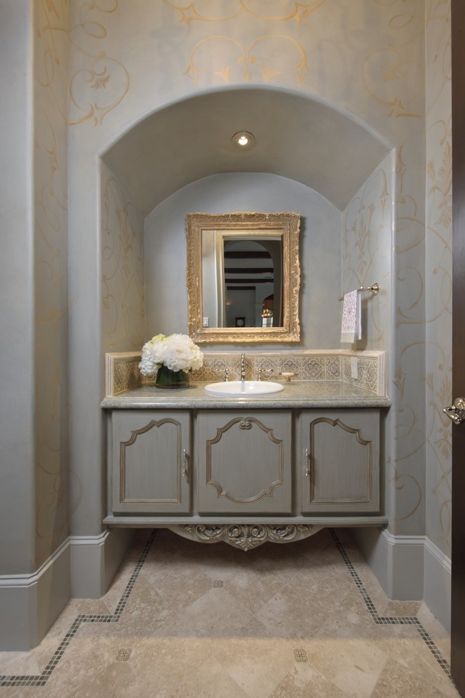 Idée de décoration pour un WC et toilettes méditerranéen avec un lavabo posé, un placard avec porte à panneau encastré, des portes de placard grises et un carrelage beige.