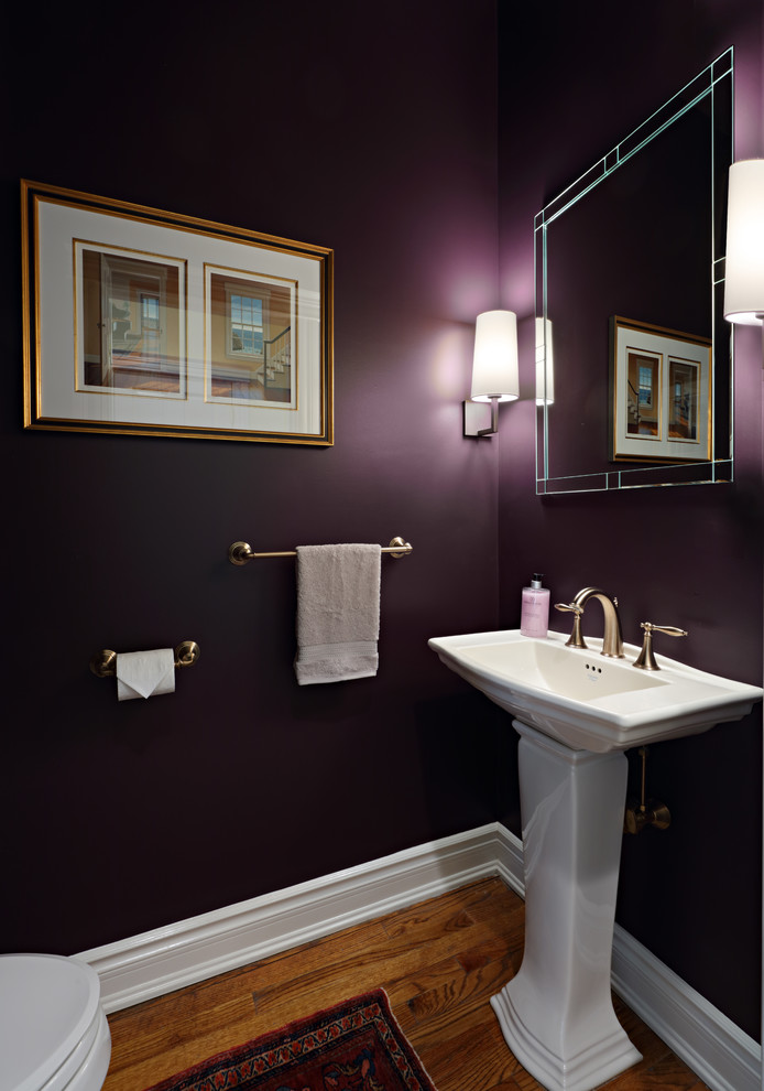 Small elegant medium tone wood floor and brown floor powder room photo in New York with a one-piece toilet, purple walls and a pedestal sink