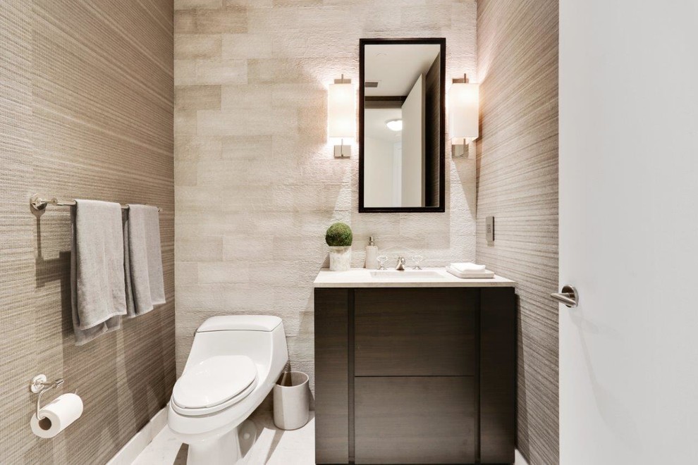 Cette image montre un petit WC et toilettes design en bois foncé avec un placard à porte plane, WC à poser, un carrelage gris, un carrelage de pierre, un mur gris, un sol en marbre, un lavabo encastré et un plan de toilette en marbre.