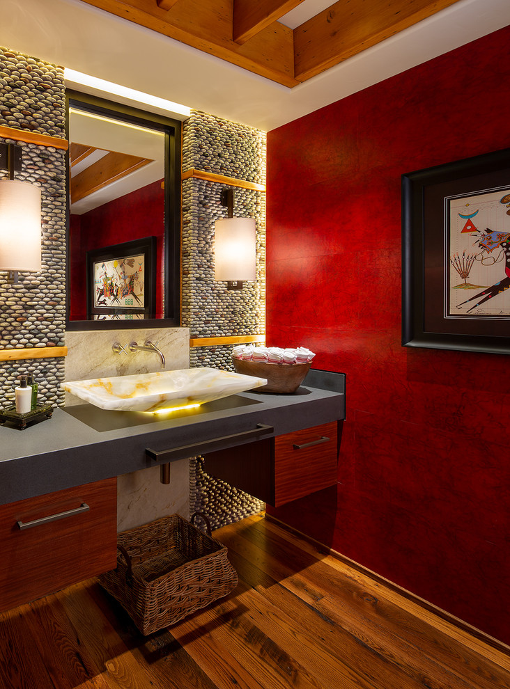 Foto på ett mellanstort rustikt grå toalett, med släta luckor, kakel i småsten, mellanmörkt trägolv, bänkskiva i täljsten, flerfärgad kakel, röda väggar och ett fristående handfat