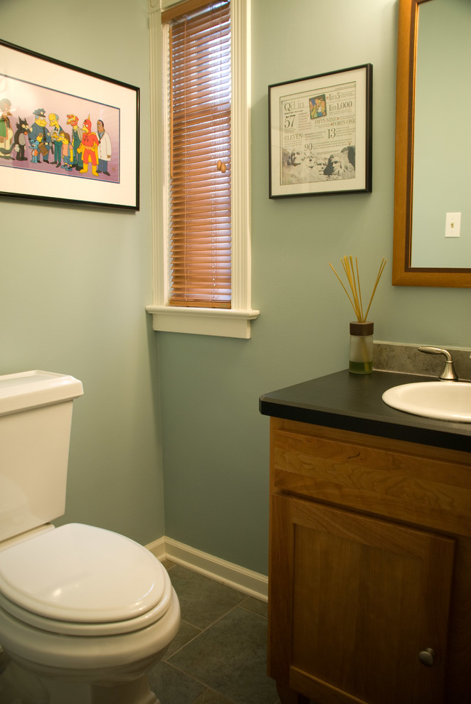 Foto på ett litet funkis toalett, med skåp i shakerstil, skåp i mellenmörkt trä, en toalettstol med separat cisternkåpa, grå kakel, keramikplattor, gröna väggar, klinkergolv i porslin, ett nedsänkt handfat och laminatbänkskiva