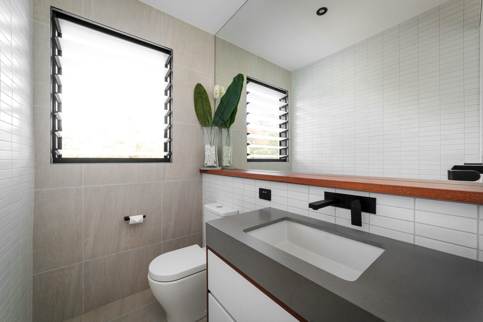 Mittelgroße Moderne Gästetoilette mit flächenbündigen Schrankfronten, grauen Schränken, Wandtoilette mit Spülkasten, Keramikfliesen, weißer Wandfarbe, hellem Holzboden, Einbauwaschbecken, Beton-Waschbecken/Waschtisch, grauem Boden und grauer Waschtischplatte in Brisbane