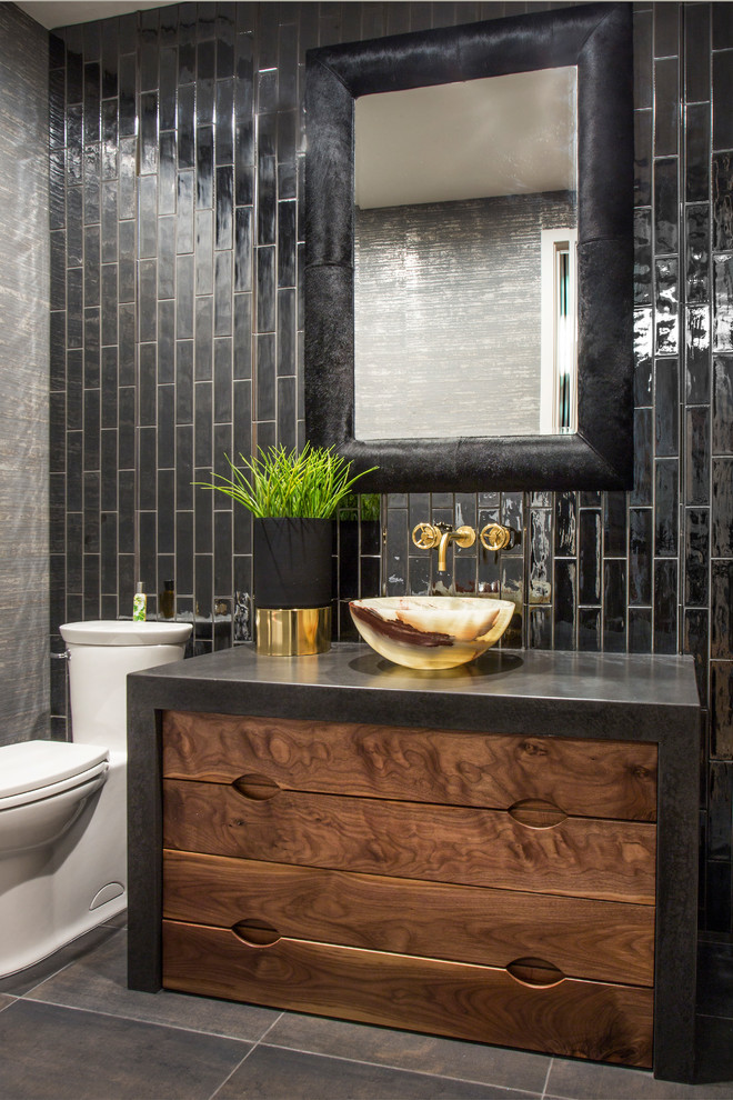 Inredning av ett industriellt svart svart toalett, med skåp i mörkt trä, en toalettstol med hel cisternkåpa, svart kakel, svarta väggar, ett fristående handfat och svart golv