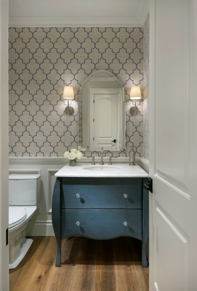 Powder room - mid-sized mediterranean wainscoting, wallpaper and beige floor powder room idea in Phoenix with blue cabinets, furniture-like cabinets, a two-piece toilet, multicolored walls, an undermount sink, white countertops and a built-in vanity