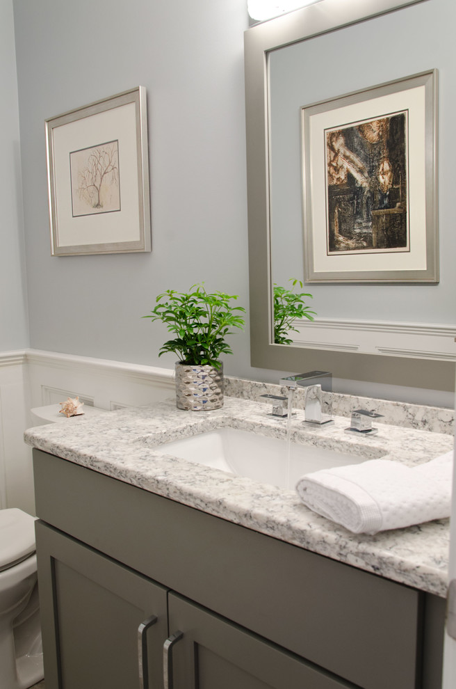 Inredning av ett klassiskt litet toalett, med luckor med infälld panel, grå skåp, en toalettstol med hel cisternkåpa, blå väggar, kalkstensgolv, ett undermonterad handfat, bänkskiva i kvarts och grått golv