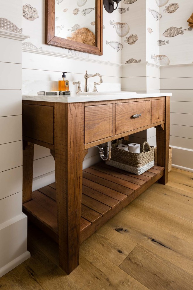 Modelo de aseo rústico de tamaño medio con lavabo encastrado, armarios tipo mueble, puertas de armario de madera oscura, encimera de mármol y suelo de madera clara