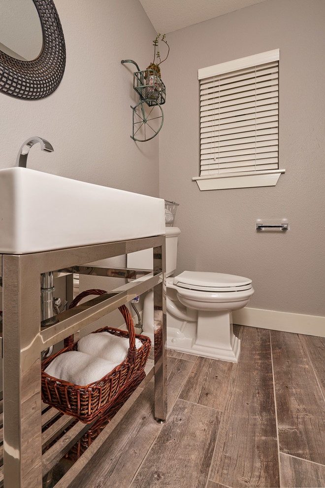 Inspiration for a small classic cloakroom in Austin with a two-piece toilet, grey walls, medium hardwood flooring, a console sink and brown floors.