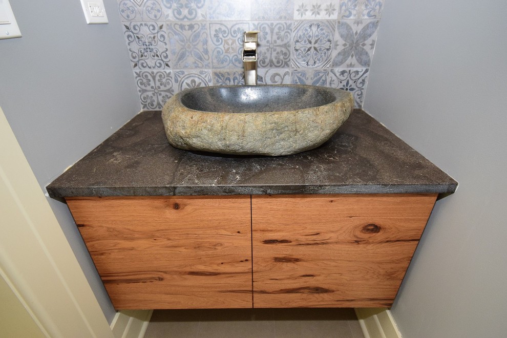 Exempel på ett nordiskt toalett, med släta luckor, skåp i mellenmörkt trä, grå kakel, keramikplattor, grå väggar, klinkergolv i porslin, ett fristående handfat, bänkskiva i täljsten och grått golv