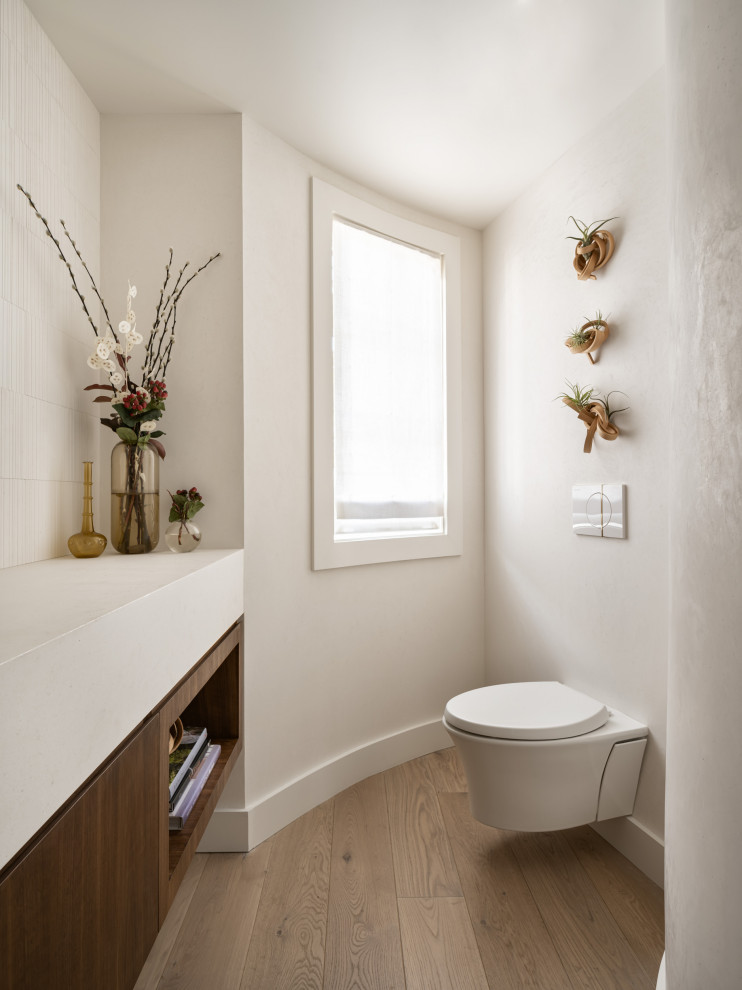Mid-sized minimalist white tile and limestone tile light wood floor and beige floor powder room photo in San Francisco with flat-panel cabinets, medium tone wood cabinets, a wall-mount toilet, white walls, an undermount sink, limestone countertops, white countertops and a floating vanity