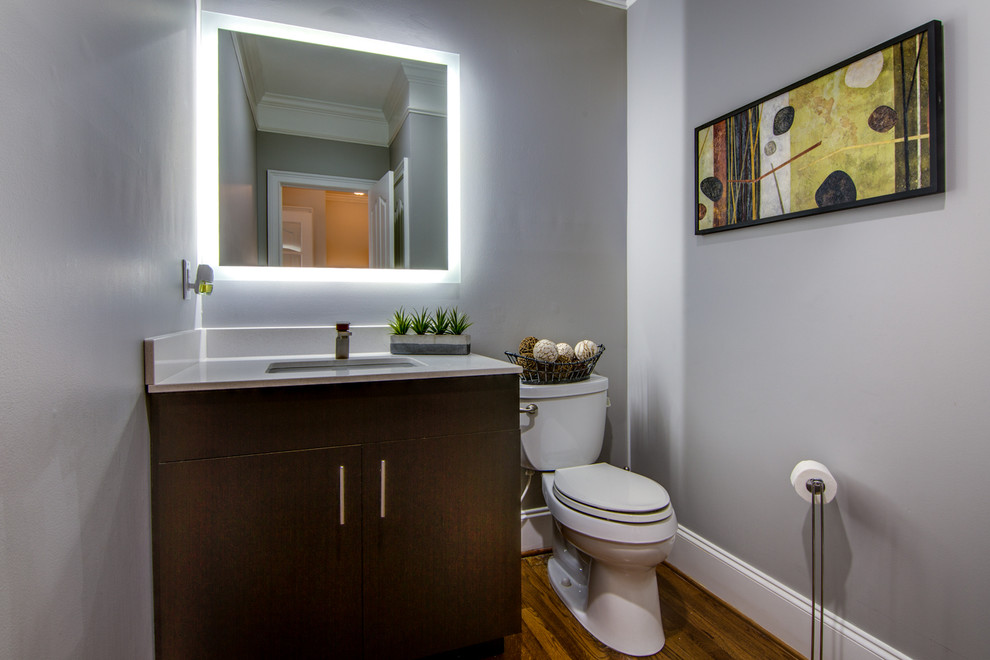 Exemple d'un WC et toilettes tendance en bois foncé avec un placard à porte plane, WC séparés, un mur gris, un lavabo encastré, un sol en bois brun et un plan de toilette blanc.