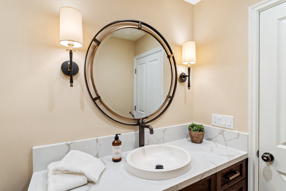 Cette image montre un grand WC suspendu traditionnel avec un placard avec porte à panneau encastré, des portes de placard marrons, un mur beige, un sol en travertin, une vasque, un plan de toilette en quartz modifié, un sol beige, un plan de toilette blanc et meuble-lavabo encastré.