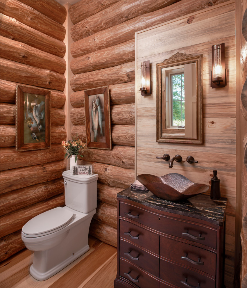 Cette image montre un WC et toilettes chalet en bois foncé et bois avec un placard en trompe-l'oeil, un sol en bois brun, une vasque, un sol marron et un plan de toilette noir.