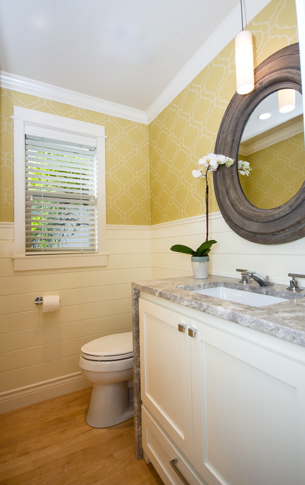 Exempel på ett litet klassiskt grå grått toalett, med ett undermonterad handfat, vita skåp, granitbänkskiva, en toalettstol med separat cisternkåpa, gula väggar, ljust trägolv och luckor med infälld panel