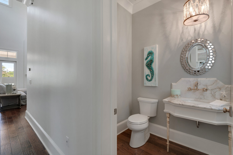 Foto på ett litet maritimt toalett, med en toalettstol med separat cisternkåpa, flerfärgad kakel, stenhäll, grå väggar, mellanmörkt trägolv, marmorbänkskiva och ett undermonterad handfat