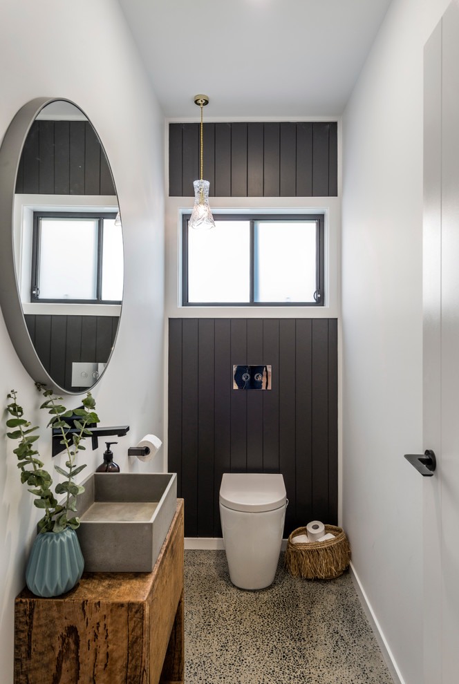 Aménagement d'un WC et toilettes bord de mer en bois brun avec un placard à porte plane, WC à poser, un mur blanc, sol en béton ciré, une vasque, un plan de toilette en bois et un plan de toilette marron.