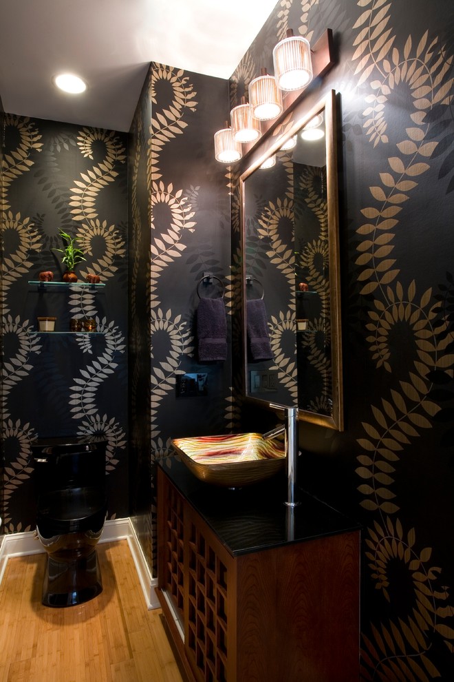Modern inredning av ett mellanstort toalett, med en toalettstol med hel cisternkåpa, svarta väggar, ljust trägolv, ett fristående handfat och brunt golv