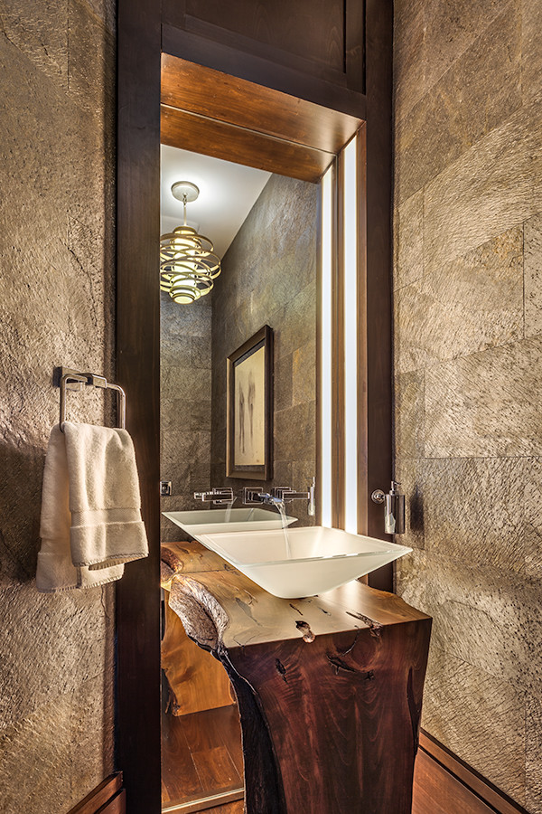 Bild på ett litet rustikt brun brunt toalett, med möbel-liknande, skåp i mörkt trä, grå kakel, grå väggar, mellanmörkt trägolv, ett fristående handfat, träbänkskiva, cementkakel och brunt golv