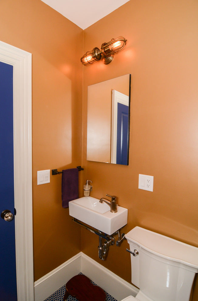 This is an example of a small rustic cloakroom in Boston with shaker cabinets, medium wood cabinets, a two-piece toilet, orange walls, mosaic tile flooring, a wall-mounted sink and blue floors.